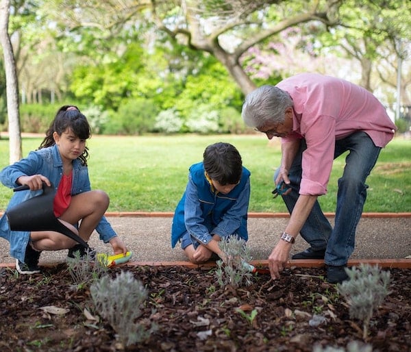 Two children water plants while an older man helps